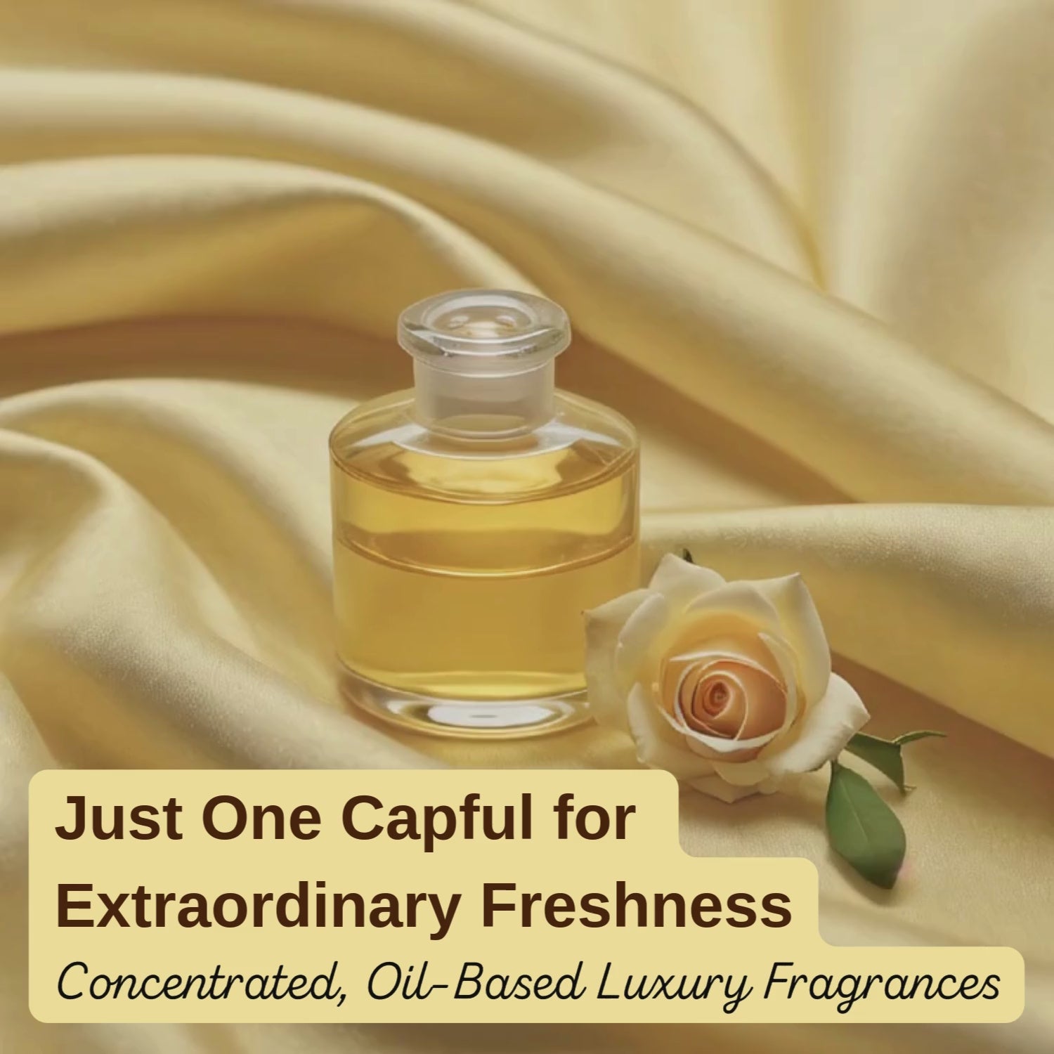 Small glass bottle of golden laundry perfume resting on soft gold satin fabric, styled with a peach rose for a luxurious freshness aesthetic.